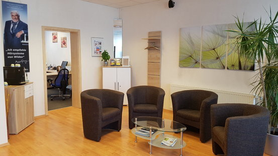 Moderner Wartebereich mit vier Sesseln, Glastisch, Pflanzen und freundlicher Büroatmosphäre.